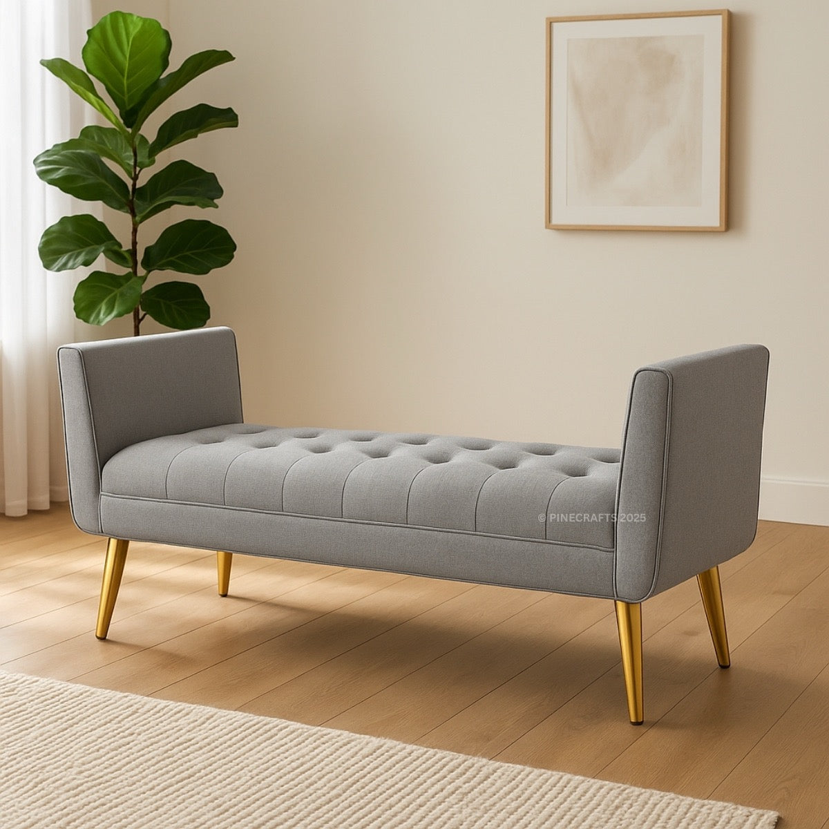 Gray tufted bench with gold legs in a room with a plant and framed picture on the wall.